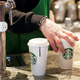 The hands of a Starbucks barista holding Starbucks single-use coffee cups